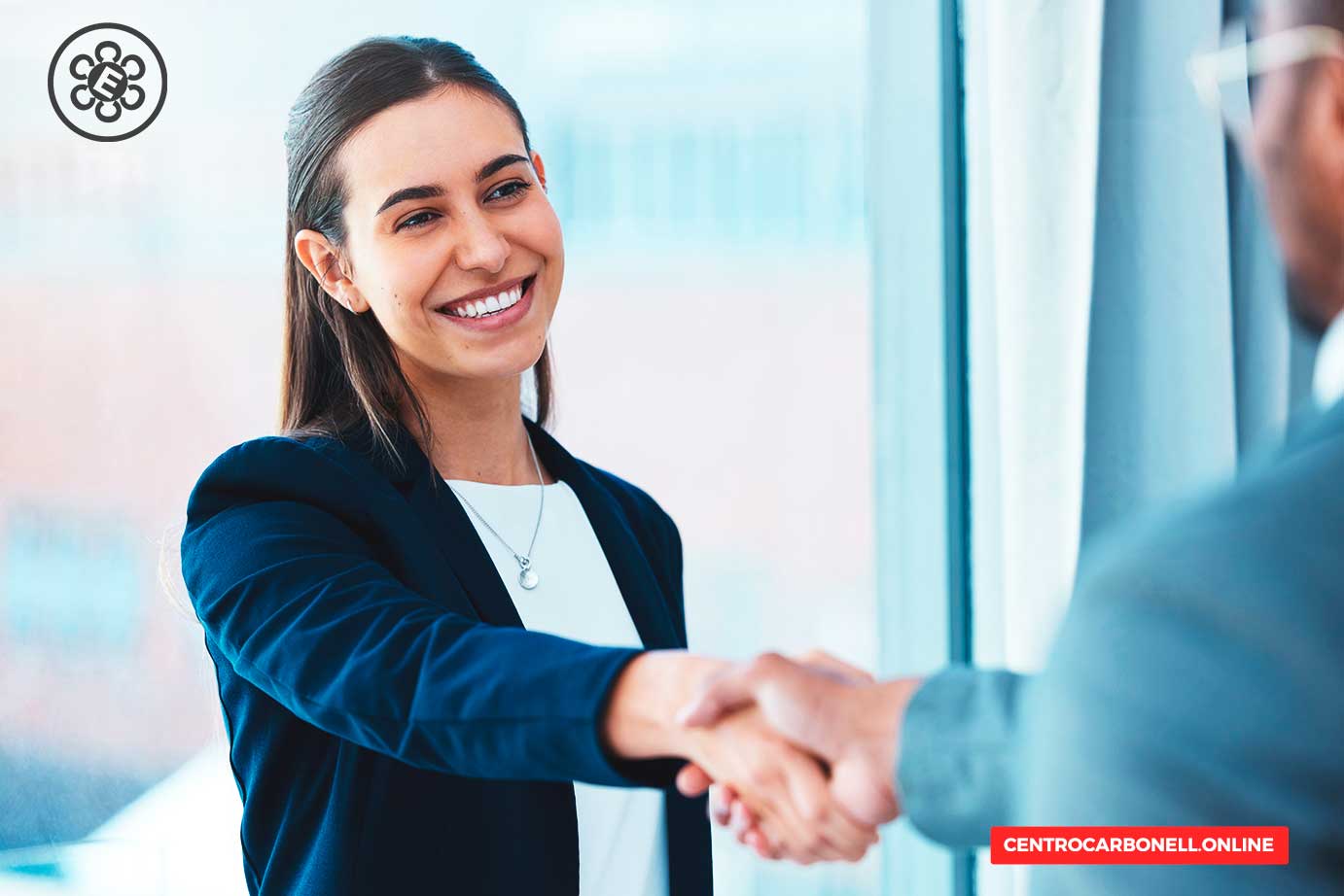 Una mujer sonriente en un entorno profesional, estrechando la mano de otro individuo con una expresión amigable, simbolizando el inicio de una colaboración o acuerdo.