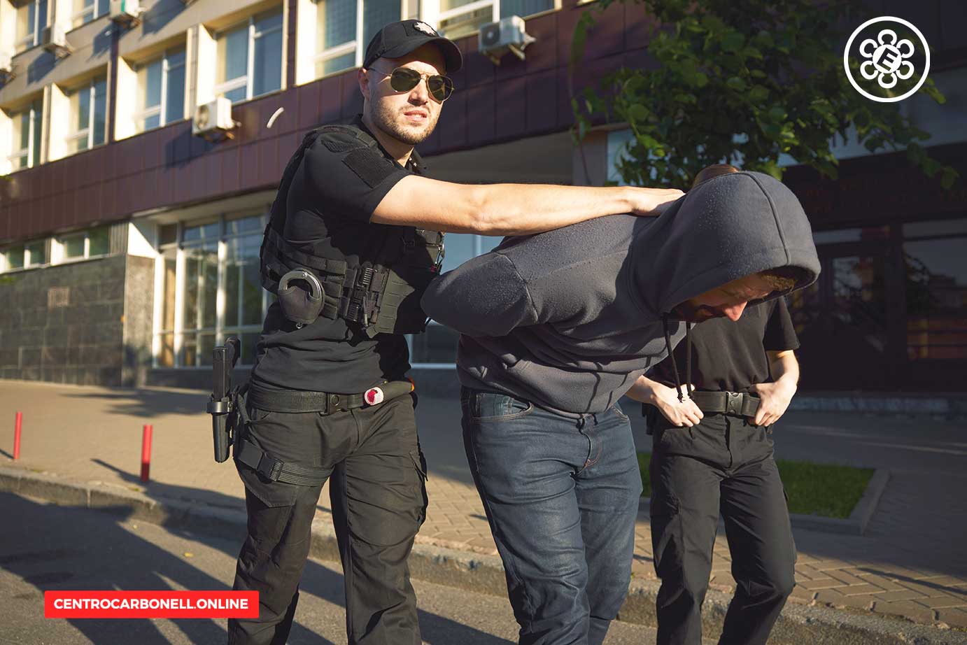 Agentes de seguridad deteniendo a un individuo, con un segundo agente observando en un entorno urbano.