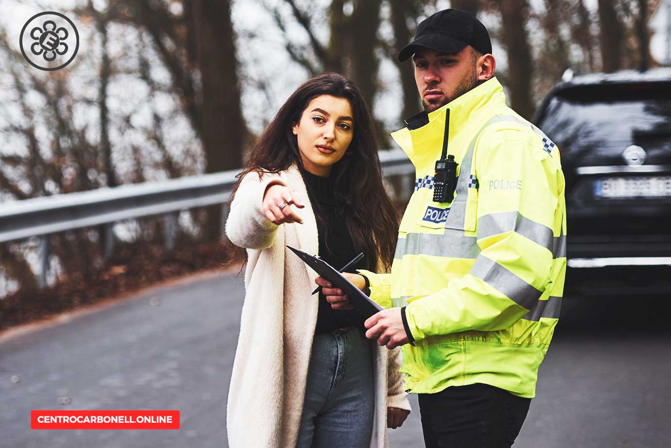 Mujer hablando con un oficial de policía en una carretera, con el oficial sosteniendo una libreta y una radio en su uniforme.