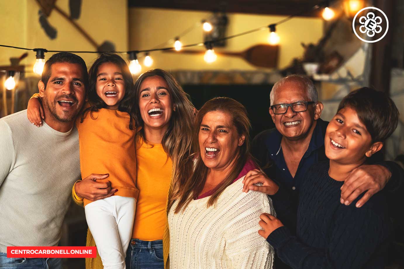 Grupo de seis personas sonriendo y posando juntas en un ambiente acogedor, con luces decorativas en el fondo.
