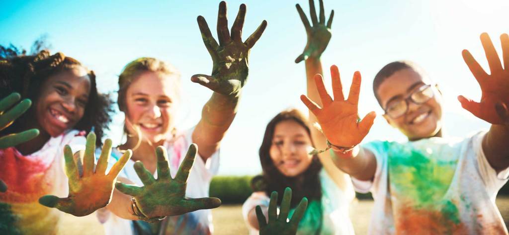 Niños felices mostrando manos llenas de pintura de colores en un día soleado.
