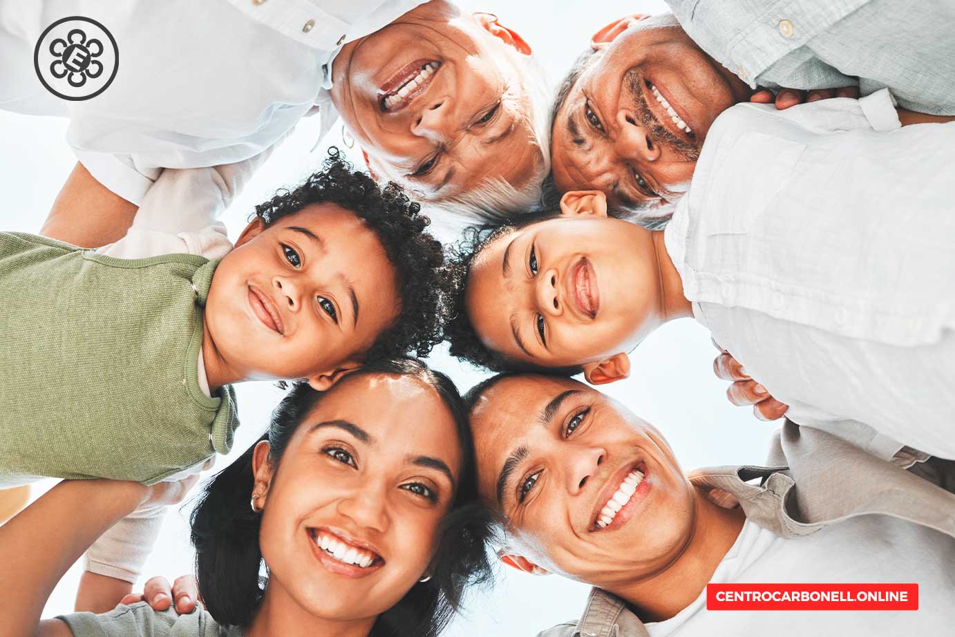 Una familia sonriente formada por varias generaciones, que incluye niños y adultos, posando en un círculo, con un ambiente alegre y acogedor.