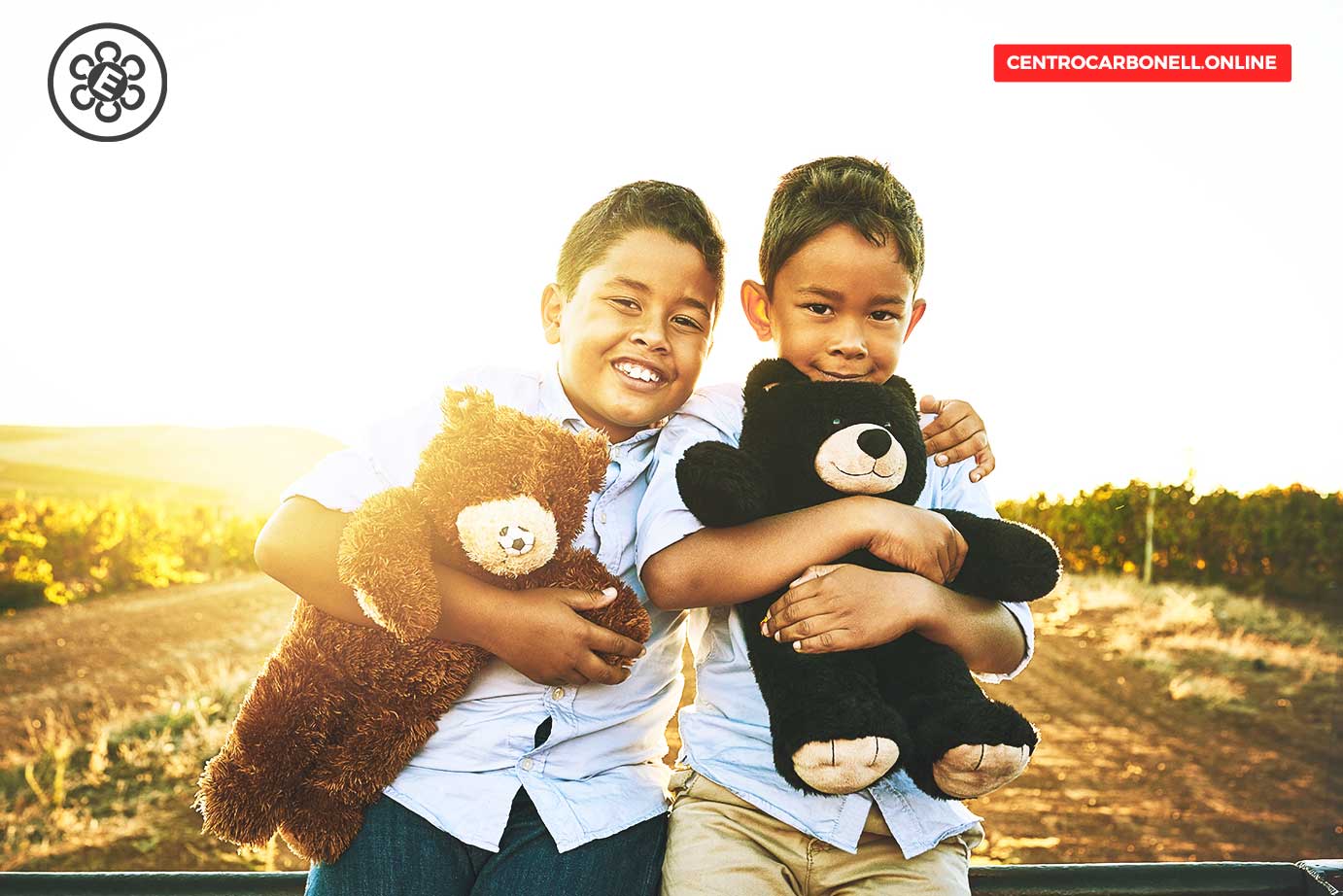 Dos niños sonriendo mientras sostienen peluches en un entorno al aire libre, con luz solar brillante al fondo.