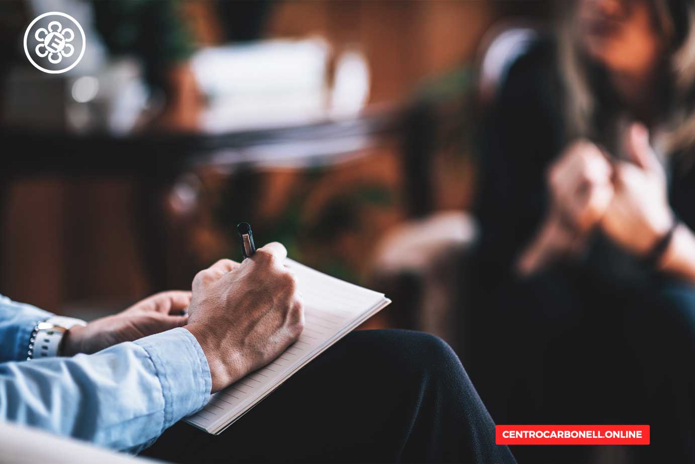 Persona tomando notas en un cuaderno durante una conversación en un entorno de evaluación o entrevista.
