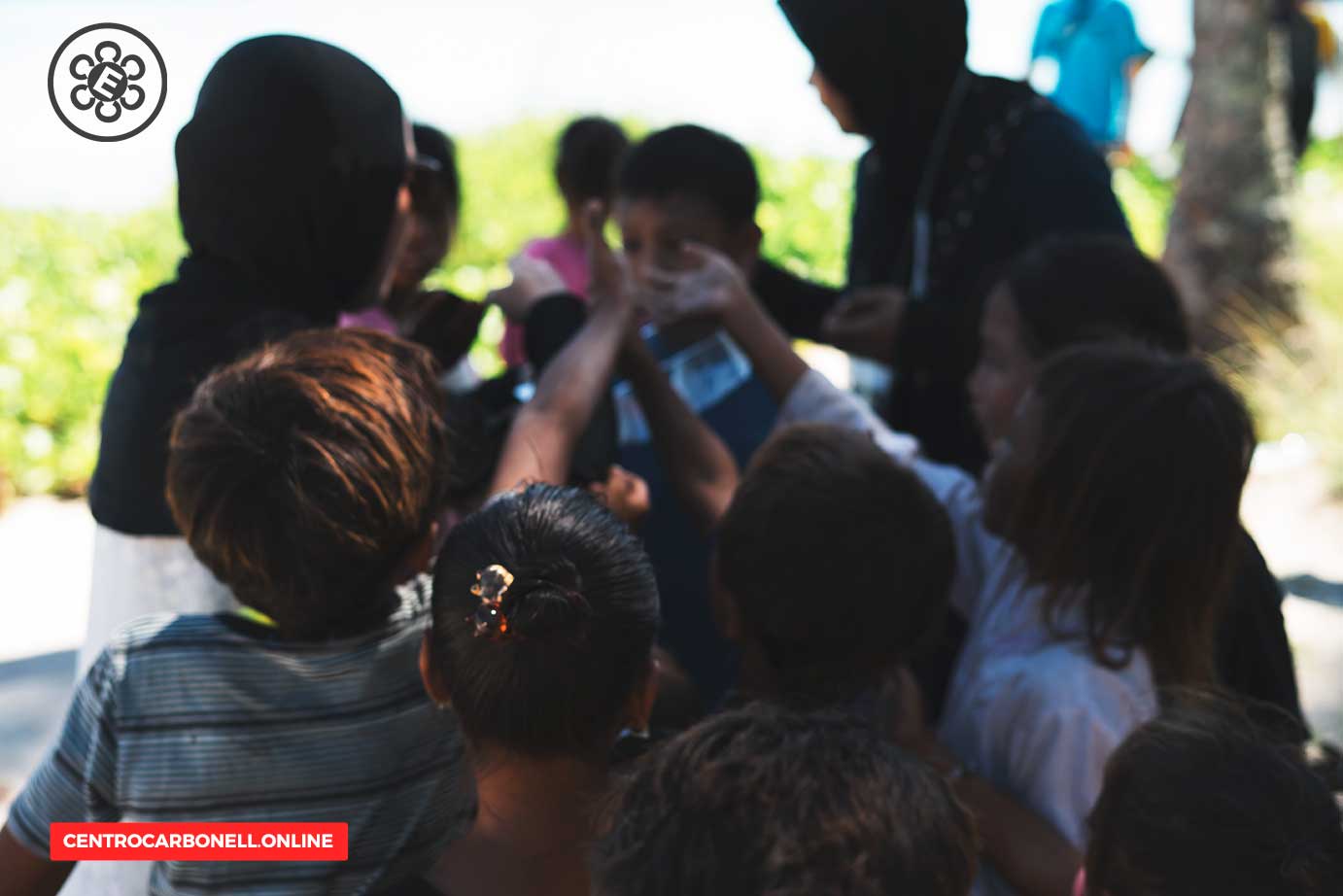 Grupo de niños interactuando en un entorno al aire libre, con una persona adulta supervisando la actividad.