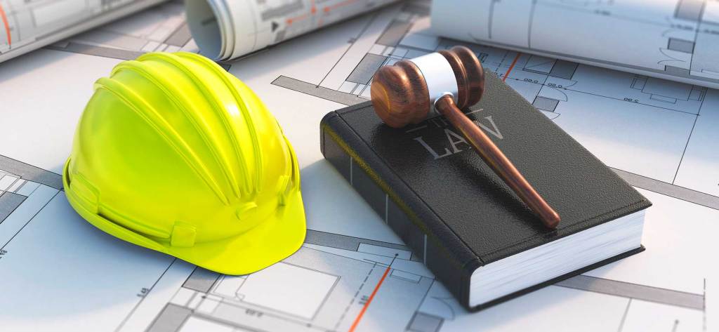 Un casco de seguridad amarillo, un libro de leyes y un mazo de juez sobre un plano arquitectónico.