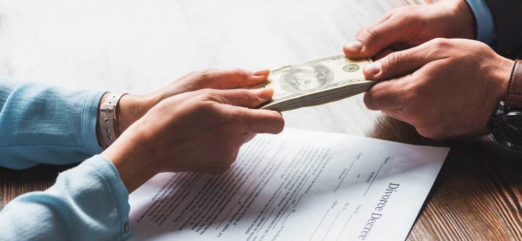 Mano entregando dinero a otra mano, con un documento de decreto de divorcio en la mesa.