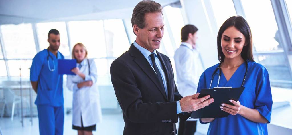 Un grupo de profesionales de la salud en un entorno hospitalario moderno, con un médico revisando documentos con una enfermera mientras otros colegas observan.