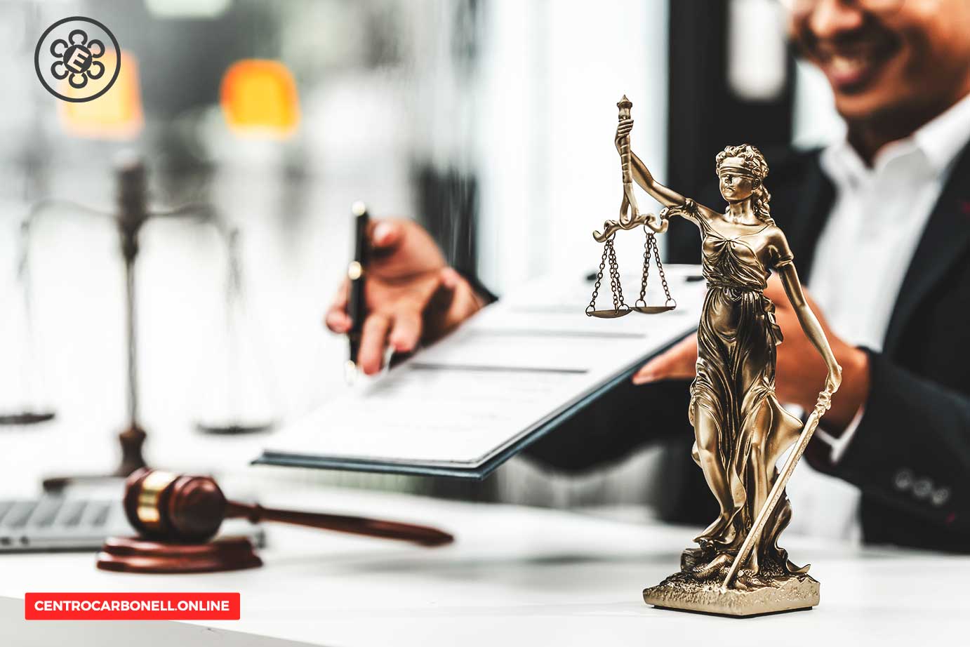 Estatua de la Justicia sosteniendo balanzas, con un hombre firmando documentos legales en un escritorio de oficina.