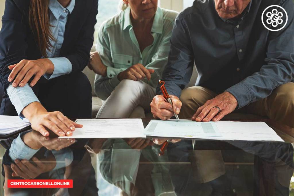 Grupo de personas revisando y firmando documentos legales sobre una mesa de vidrio, representando la consulta jurídica.
