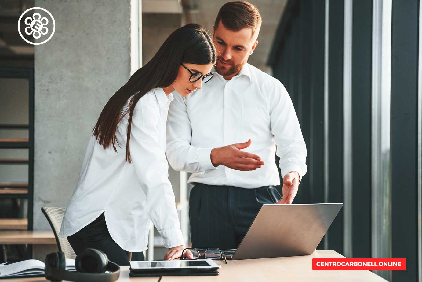 Dos profesionales colaborando en un entorno de oficina, revisando información en una laptop mientras se comunican entre sí.
