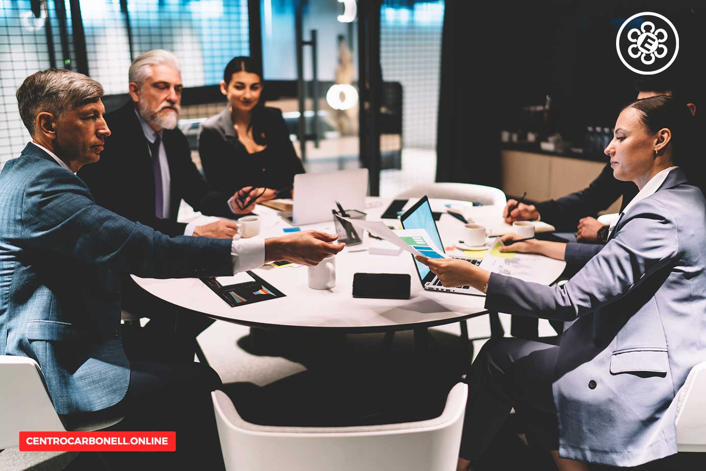 Reunión de abogados en una mesa de oficinas modernas, discutiendo documentos y usando tecnología, con un enfoque en la colaboración profesional.