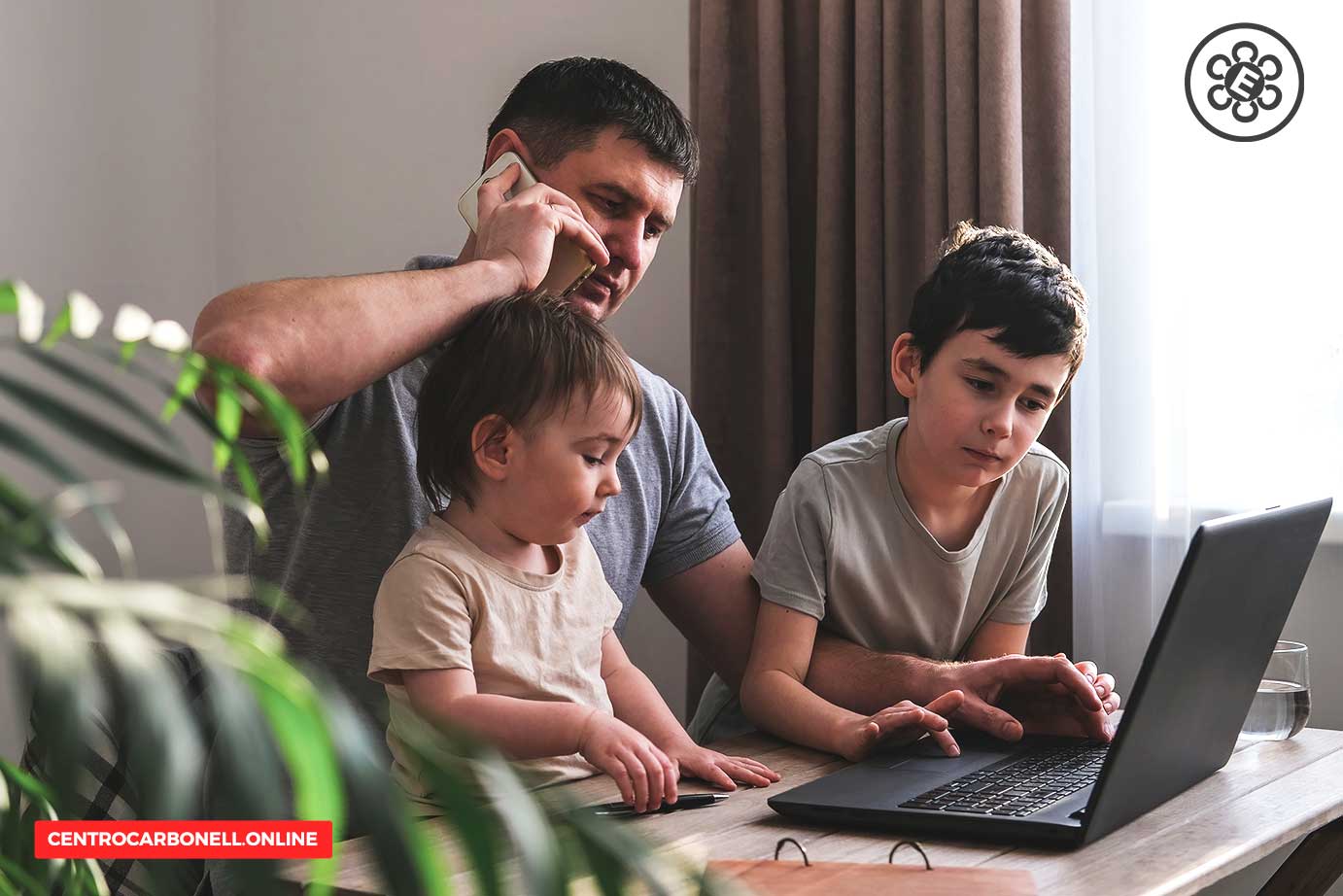 Hombre hablando por teléfono mientras trabaja en una computadora portátil con dos niños pequeños a su lado en un entorno doméstico.
