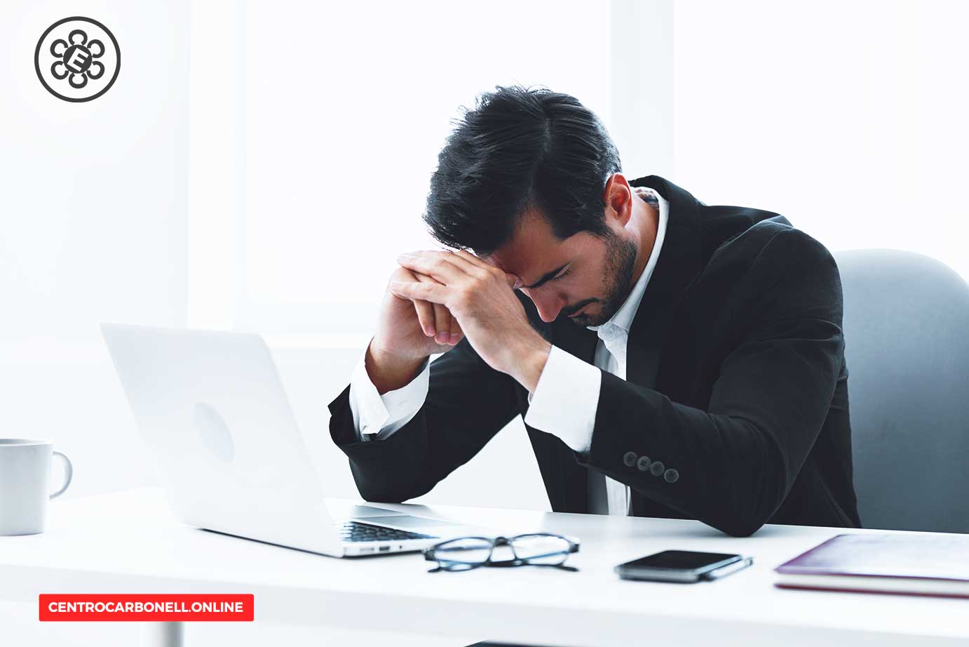 Hombre con traje sentado frente a una computadora, con las manos en la cabeza, reflejando preocupación o estrés en un entorno de oficina.