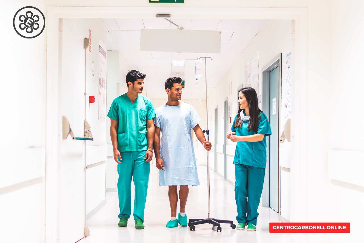 Hospital interior showing a patient in a hospital gown walking with two medical staff, one male and one female, in scrubs, in a modern corridor.