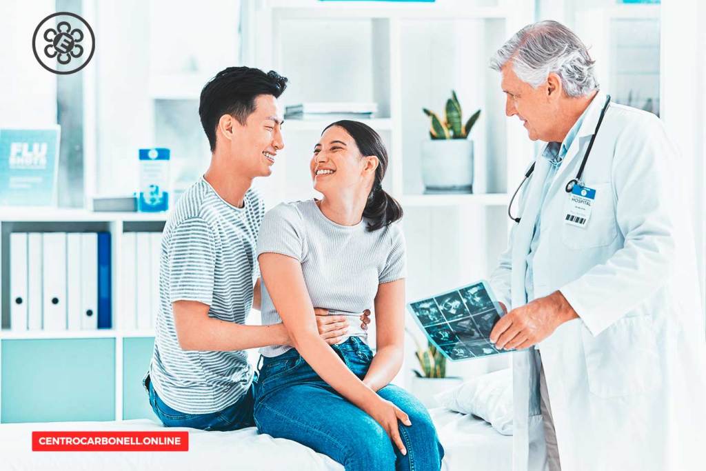 Una pareja sonriente sentada en una consulta médica, acompañada por un doctor que sostiene un informe o imágenes, dentro de un ambiente clínico luminoso.