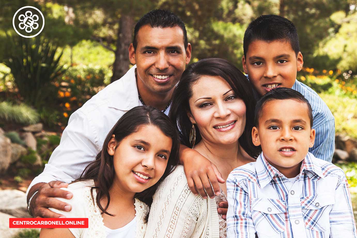 Familia sonriente posando en un entorno natural, con dos adultos y tres niños, todos vestidos de manera casual.