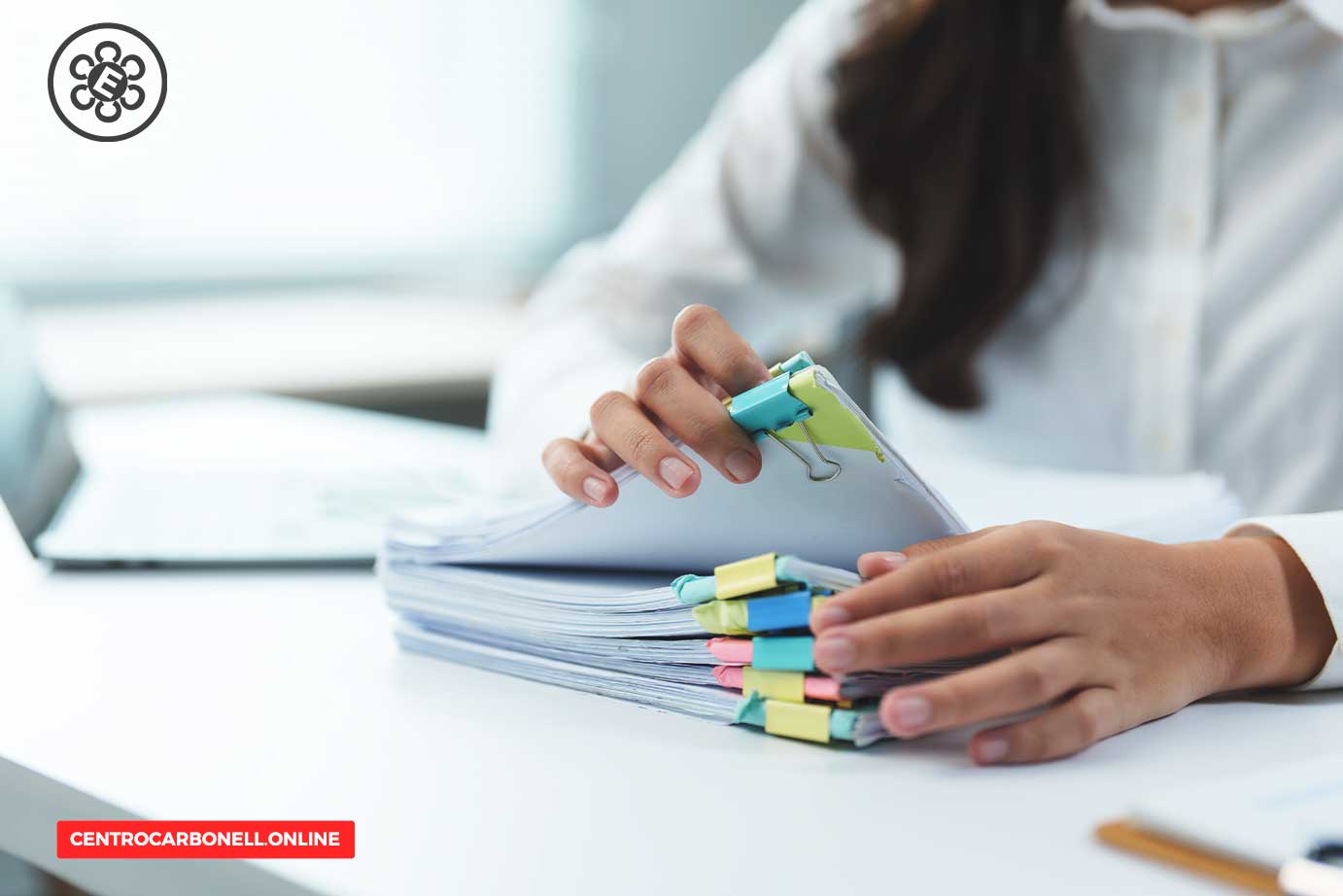 Close-up of a person's hands organizing a stack of documents secured with colorful clips on a desk.