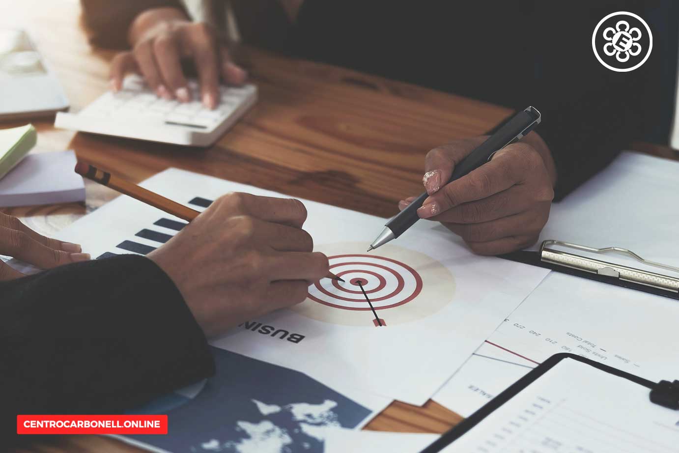 Dos personas analizando gráficos y un objetivo en una hoja de papel sobre una mesa de madera.