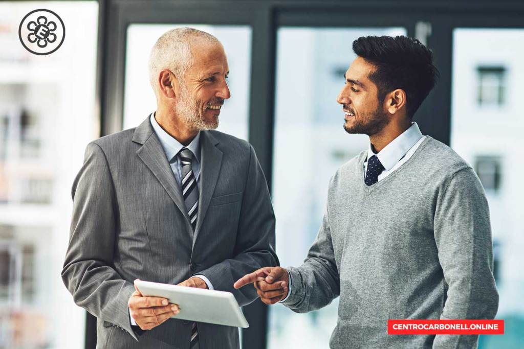 Dos hombres de negocios conversando mientras revisan una tablet en un entorno de oficina.