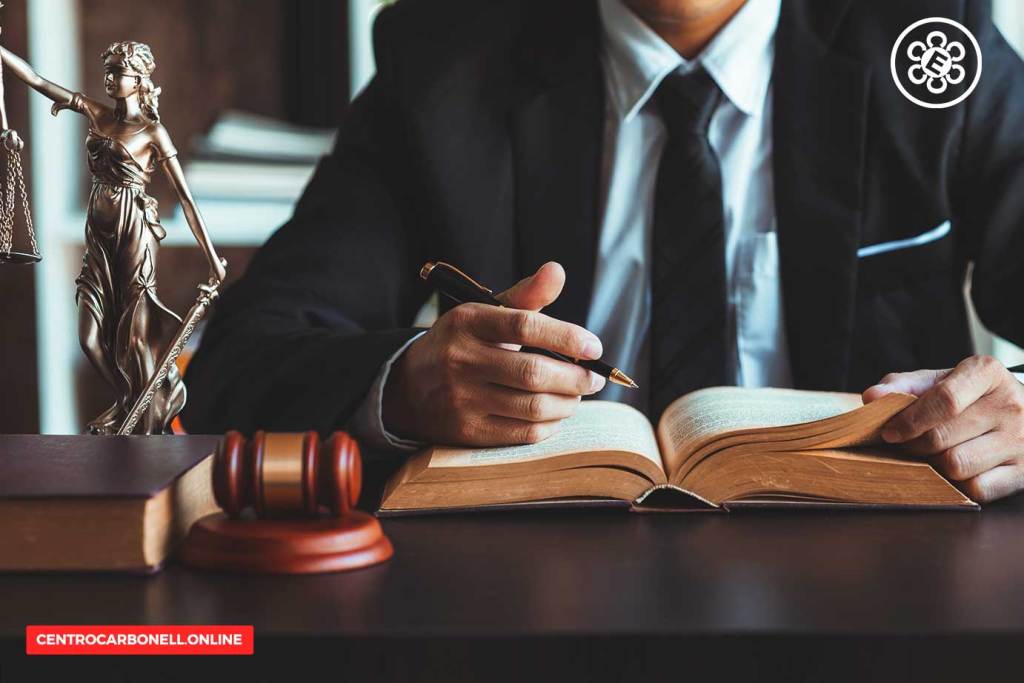 Abogado revisando un libro de leyes con una pluma, junto a un martillo y una figura de la justicia.