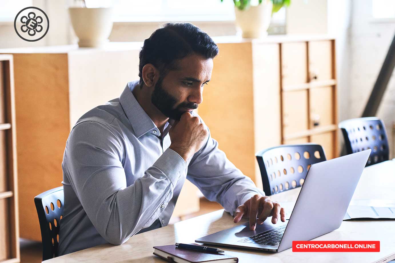 Hombre con barba, concentrado en la computadora portátil en un entorno de oficina.
