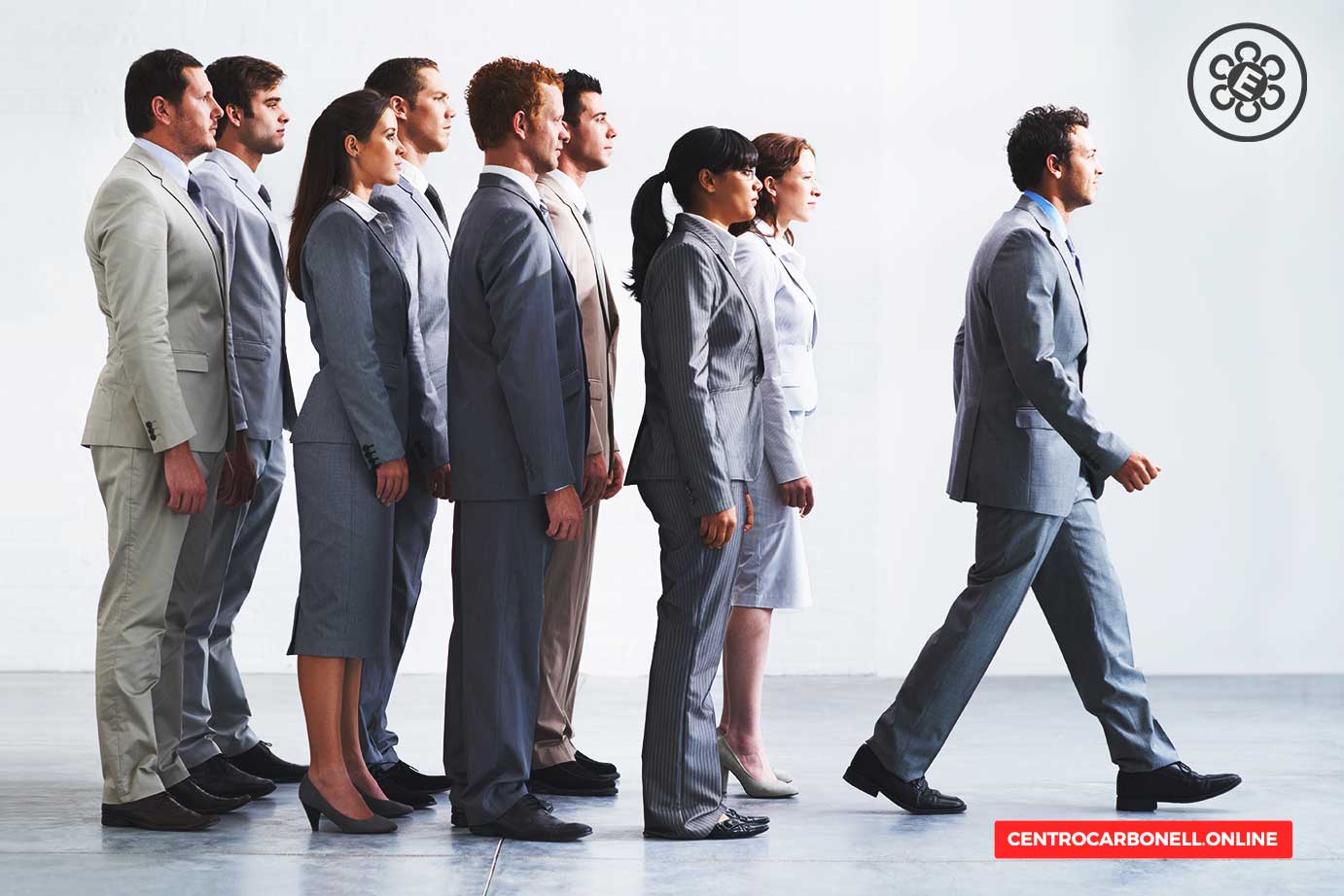 Grupo de personas vestidas formalmente alineadas en fila, con un hombre al frente caminando hacia la derecha.