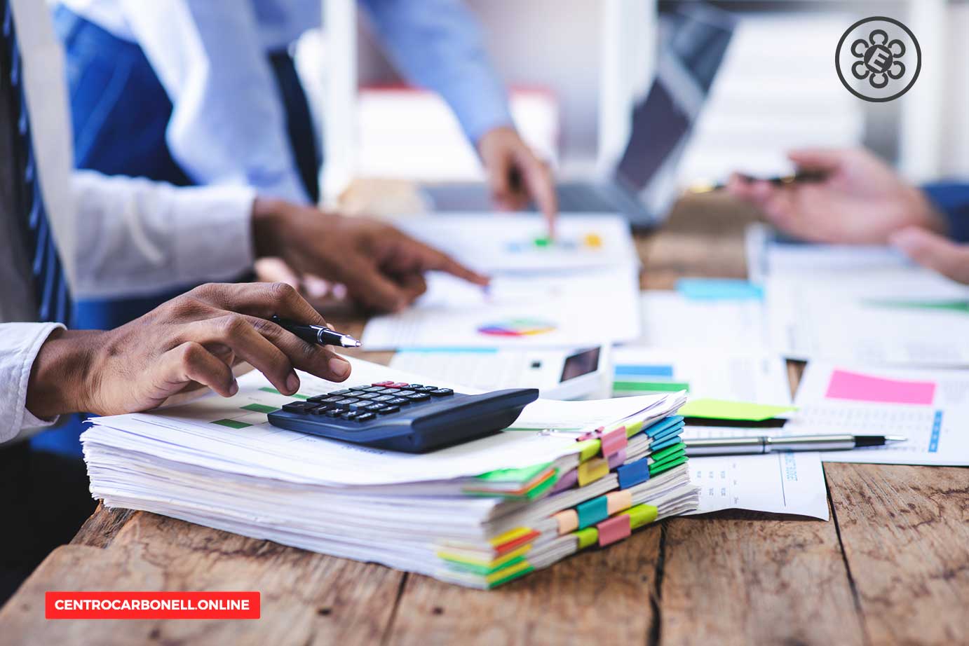 Manos de personas trabajando en documentos, hojas de papel y una calculadora en una mesa de madera.