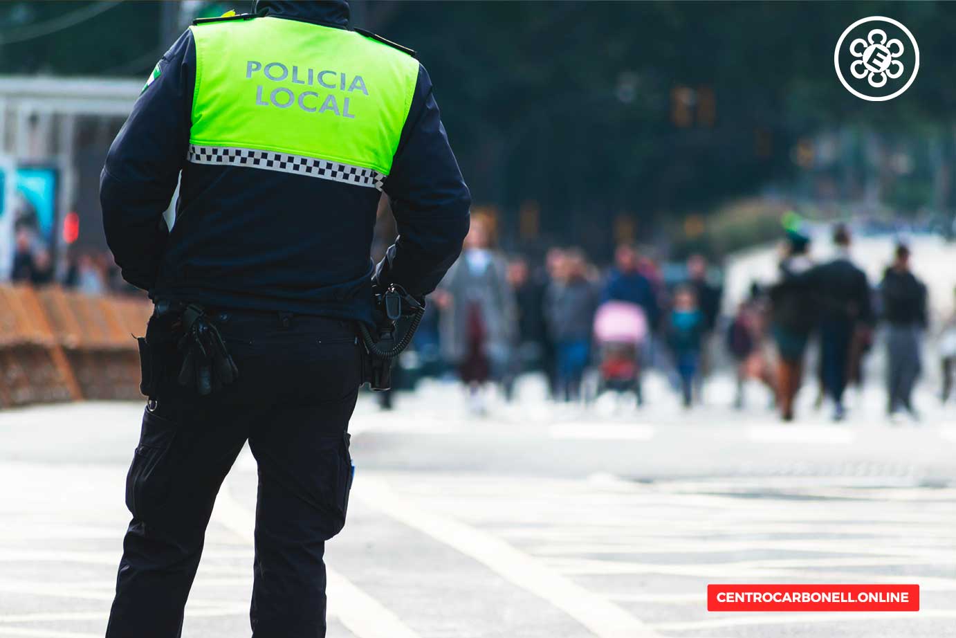 Policía local de espaldas en una calle concurrida, observando a los transeúntes.