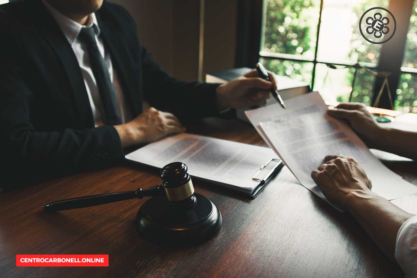Dos personas en una reunión legal revisando documentos en una mesa, con un mazo de juez en primer plano.