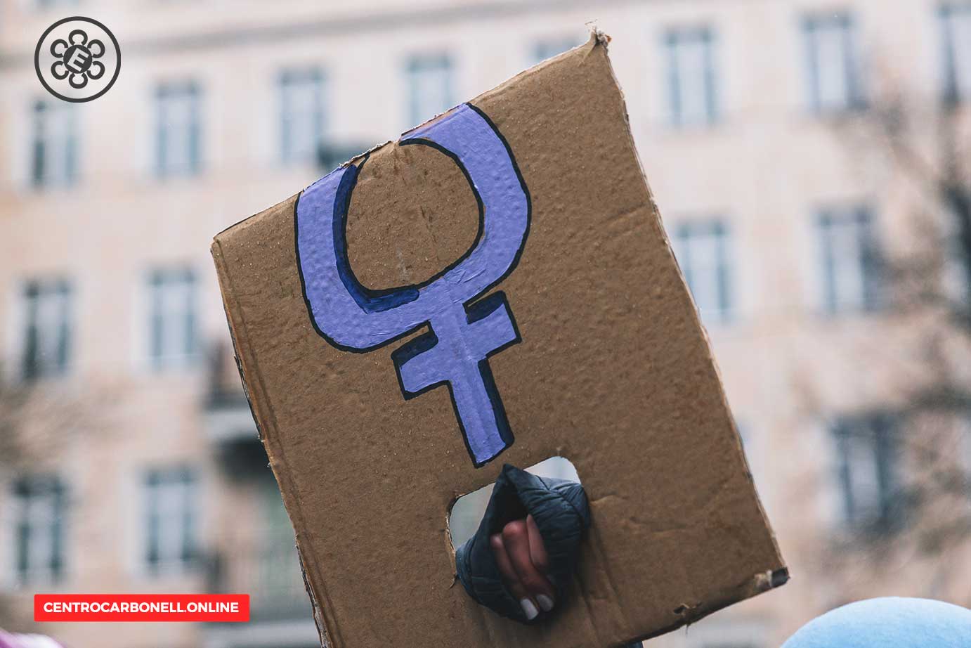 Cartón con el símbolo femenino, sostenido por una mano durante una manifestación.