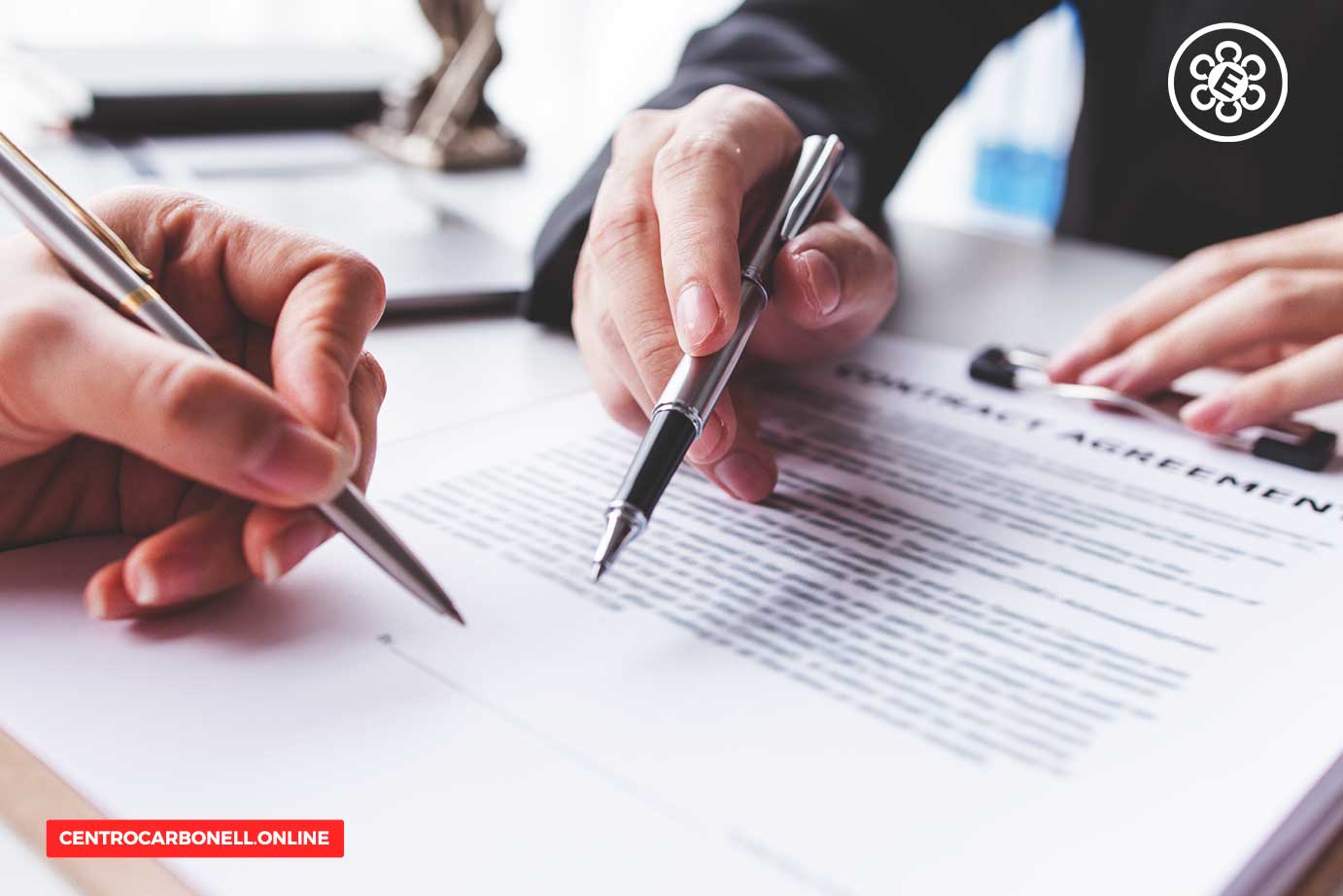 Manos firmando un contrato sobre una mesa, con un enfoque en los bolígrafos y el documento.