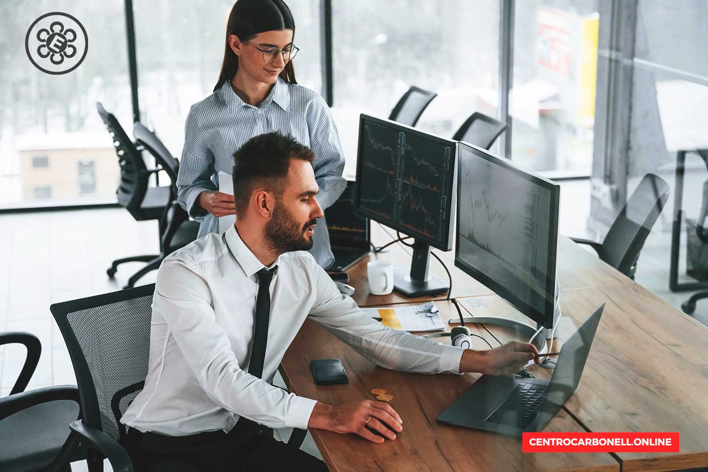 Un hombre y una mujer colaborando en un entorno de oficina moderno, con computadoras que muestran gráficos y datos financieros.