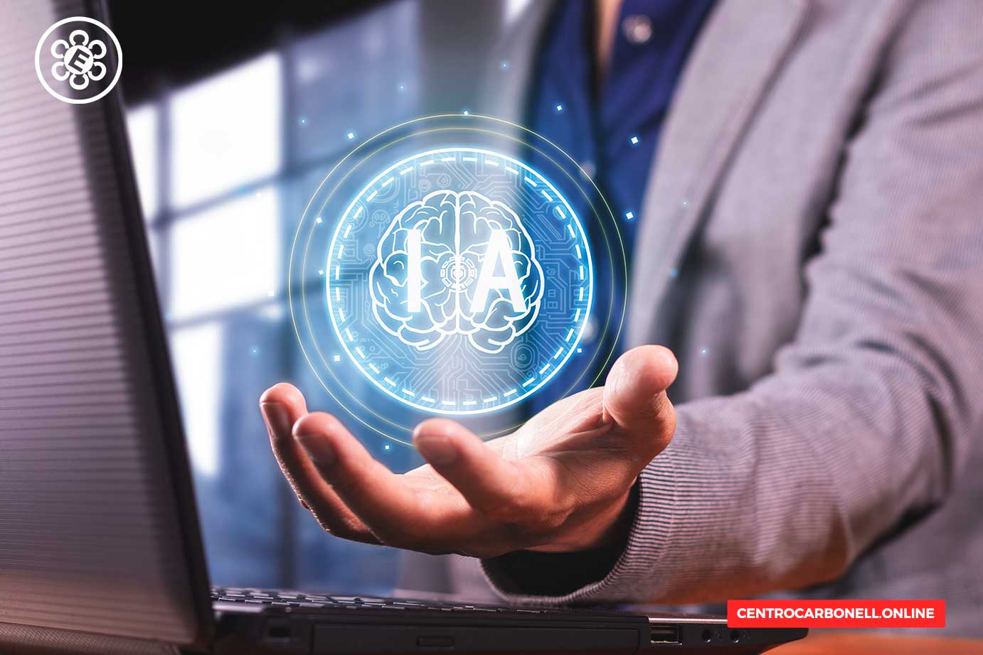 Una mano sostiene un holograma de un cerebro con la letra 'IA', simbolizando inteligencia artificial, frente a una computadora portátil.