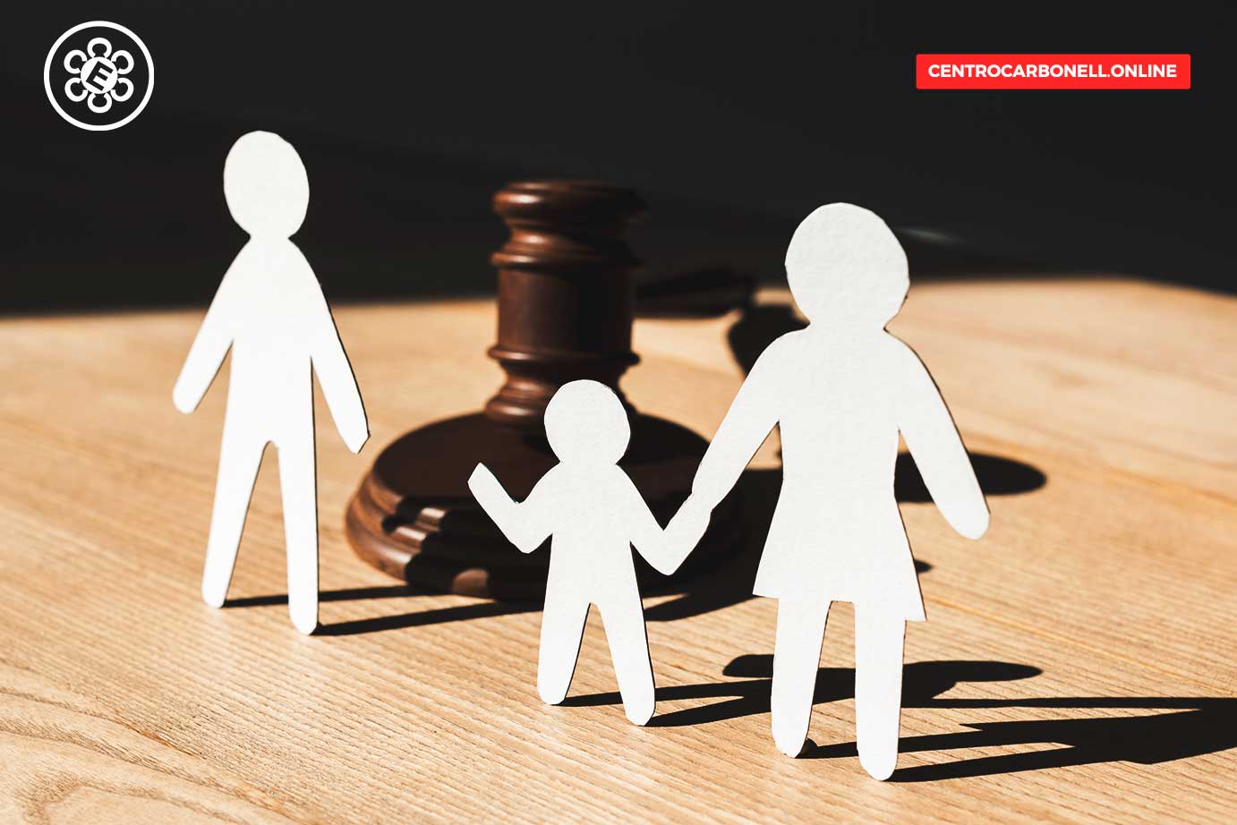 Figuras de papel representando una familia de tres personas junto a un mazo de juez sobre una mesa de madera.