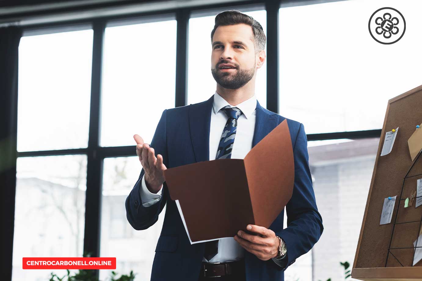 Hombre de negocios en traje sosteniendo un documento mientras presenta información en una oficina moderna.
