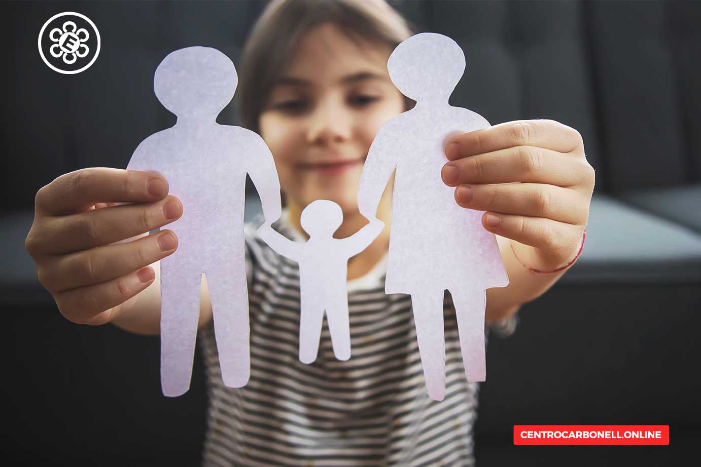Niña sosteniendo figuras recortadas de papel que representan a una familia: un padre, una madre y un niño.