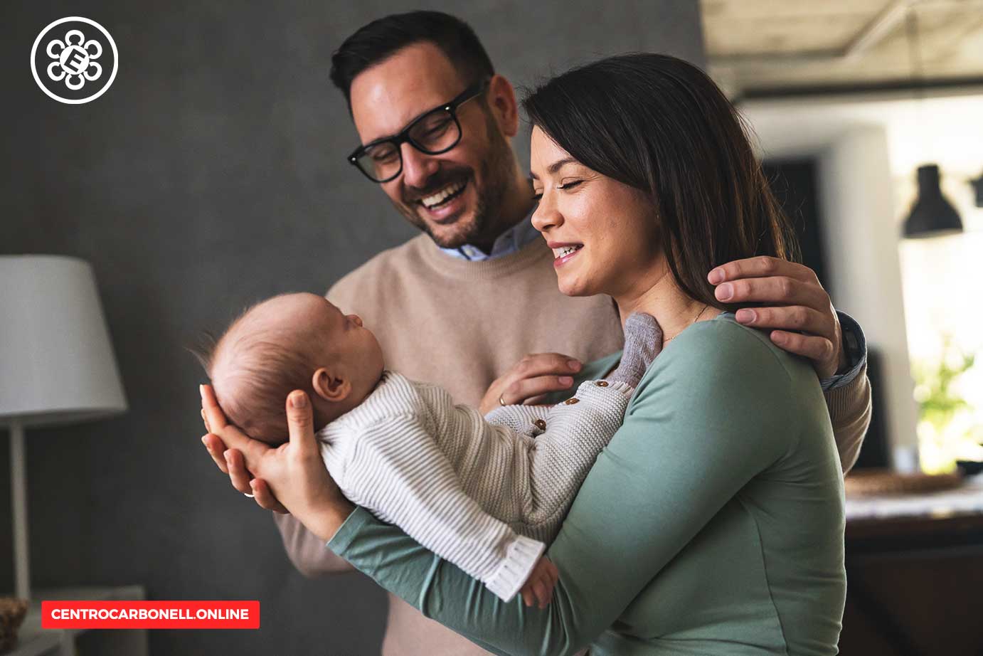 Una pareja sonriente sostiene a su bebé en un ambiente acogedor.