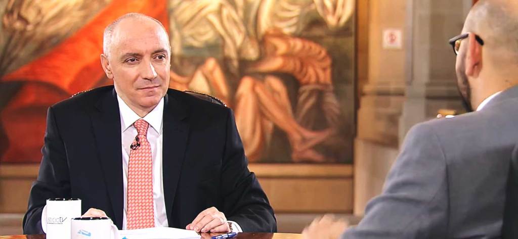 Entrevista entre dos hombres en un estudio, con un fondo artístico que muestra figuras humanas.