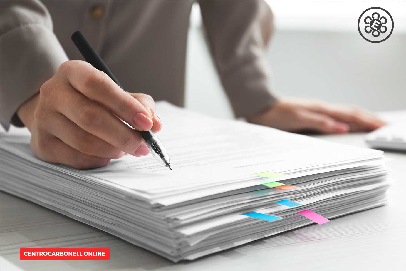 Una mano sostiene un bolígrafo sobre una pila de documentos con marcadores de colores.