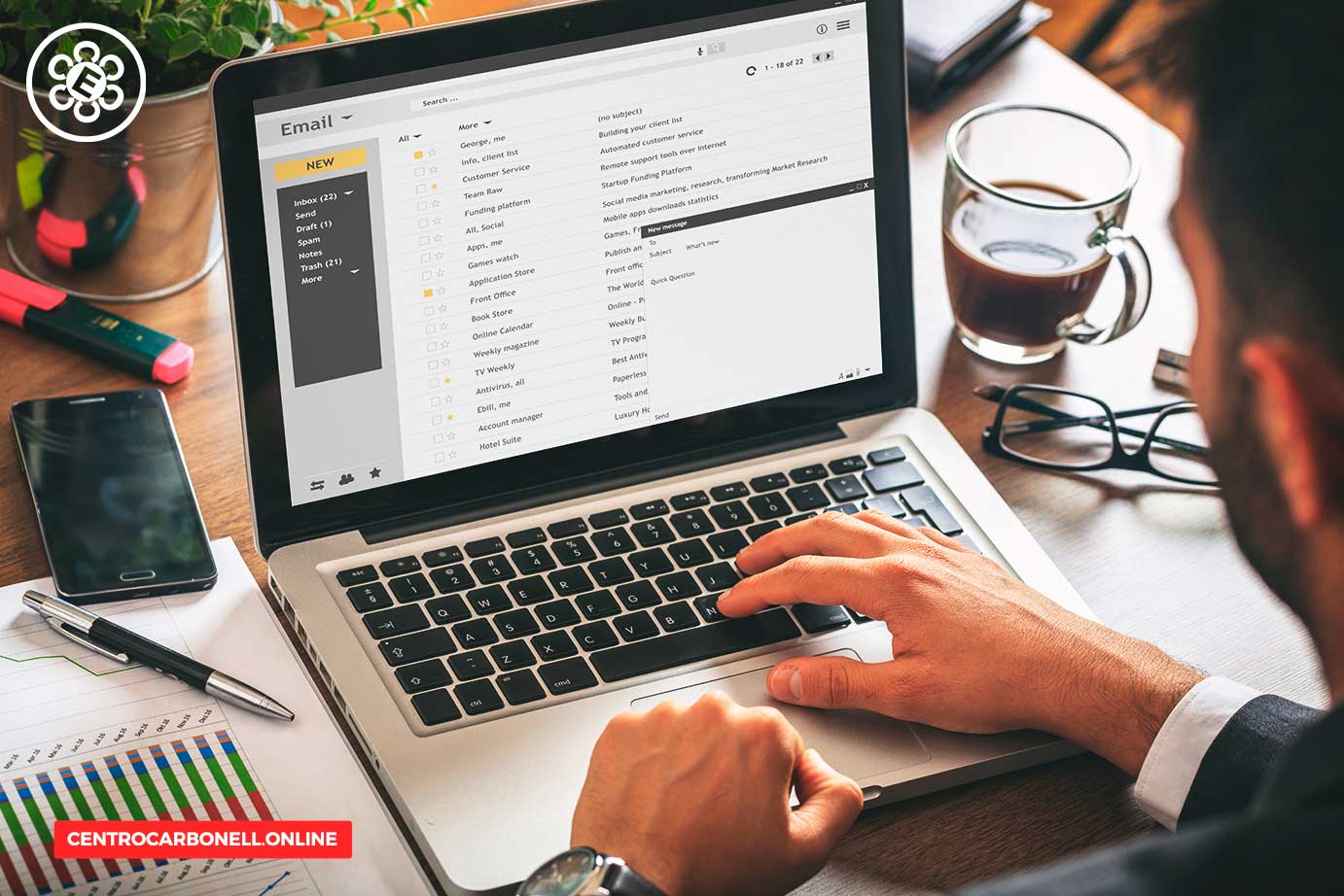 Persona utilizando una laptop con una pantalla de correo electrónico, con una taza de café y un teléfono móvil en la mesa.